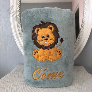 May include: A soft gray plush blanket with an embroidered lion design and the name "Come" in gold thread.