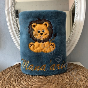 May include: A blue plush blanket with an embroidered lion and the text "Mama's" in yellow thread.
