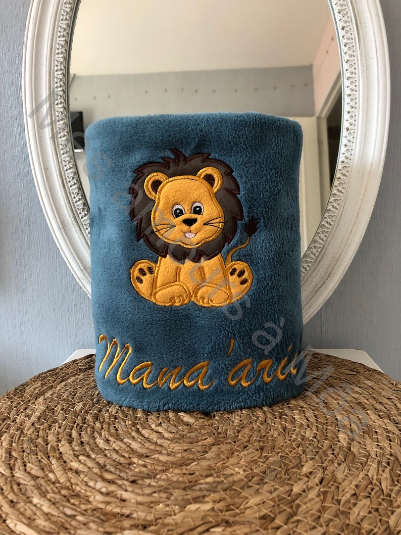May include: A blue plush blanket with an embroidered lion and the text "Mama's" in yellow thread.