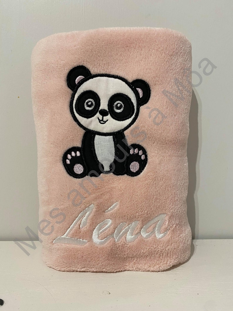 May include: A pink plush blanket with a black and white panda embroidered on it. The blanket has the name "Lena" embroidered on it in white.