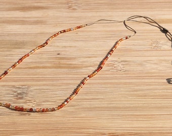 May include: A delicate necklace featuring a single strand of small, translucent beads in shades of amber, orange, and clear white. The necklace is strung on a thin, light brown cord with an adjustable sliding knot closure and small bead accents.