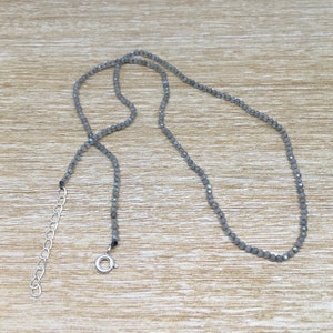 May include: A silver chain necklace with a silver clasp. The necklace is made of small, round, gray beads.