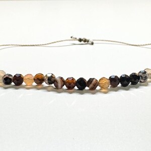 May include: A brown, black, and white agate bead necklace with a sliding knot closure.