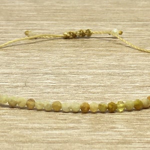 Peut inclure: Un bracelet délicat composé de petites perles rondes de pierres précieuses vert clair et jaunes. Le bracelet est réglable avec un nœud coulissant et présente un design simple et minimaliste.