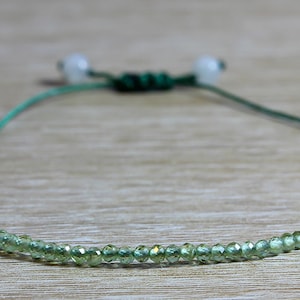 May include: A green gemstone beaded bracelet with a green cord and white knots.