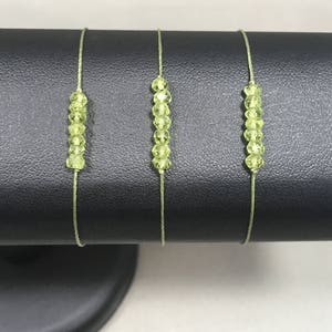 May include: Three delicate bracelets with light green gemstone beads strung on thin, light green cords. The bracelets are displayed on a black velvet stand.