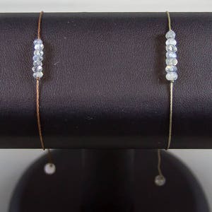 Puede incluir: Ocho pulseras delicadas con pequeñas cuentas transparentes y un colgante de amatista o piedra preciosa transparente que cuelga de cada una.