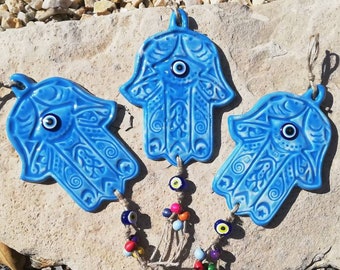 Light blue glossy ceramic hamsa wall decor with evil eye pendant, authentic oriental home protection amulet sign, boho hamsa wall hanging