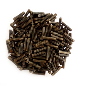 Puede incluir: Una colección de pequeñas cuentas cilíndricas de color marrón oscuro con un patrón de rayas. Las cuentas están dispuestas en forma circular sobre un fondo blanco. Estas cuentas podrían usarse para hacer joyas u otros proyectos de artesanía.