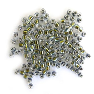 Peut inclure: Un tas de petites perles de verre transparentes avec un reflet iridescent vert.