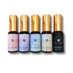 May include: Five small glass bottles with gold caps and labels that say "EarthStar Collective" and feature a star design. The bottles are arranged in a row on a white background.