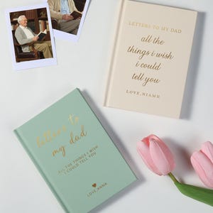 Pode incluir: Dois cadernos com letras douradas que dizem "Letters to my Dad" e "All the things I wish I could tell you". Um é verde claro, o outro creme. Duas fotos de um homem lendo e duas tulipas cor-de-rosa também estão na imagem.