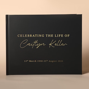 Puede incluir: Un libro de luto negro con letras doradas. En la portada se lee "CELEBRATING THE LIFE OF Caitlyn Keller" y las fechas "12th March 1950-25th August 2024". El libro cerrado tiene un acabado mate.
