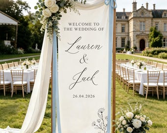 Op de afbeelding: Een verticaal welkomstbord voor een bruiloft op een houten frame met witte stof en de tekst "WELCOME TO THE WEDDING OF Lauren & Jack 26.04.2026". Het bord is versierd met witte rozen, eucalyptus en lichtblauwe linten.