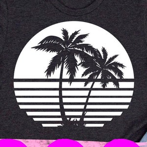 May include: A dark gray t-shirt with a white graphic of two palm trees in front of a sunset. The graphic is in a circle with white stripes.