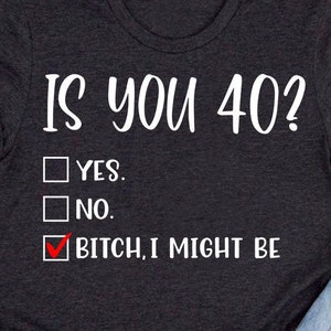 May include: A dark gray t-shirt with the text "IS YOU 40?" and a checkbox list with the options "YES", "NO", and "BITCH, I MIGHT BE". The third option is checked.