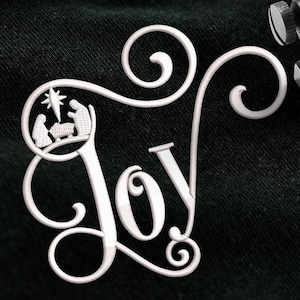 May include: A black t-shirt with white embroidery of the word "Joy" with a stylized nativity scene inside the "O". A sewing machine is stitching the embroidery.