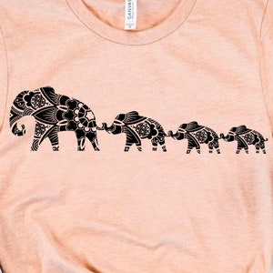 Może przedstawiać: Różowy t-shirt z czarną sylwetką rodziny słoni idących w szeregu. Słonie są ozdobione skomplikowanymi wzorami mandali.