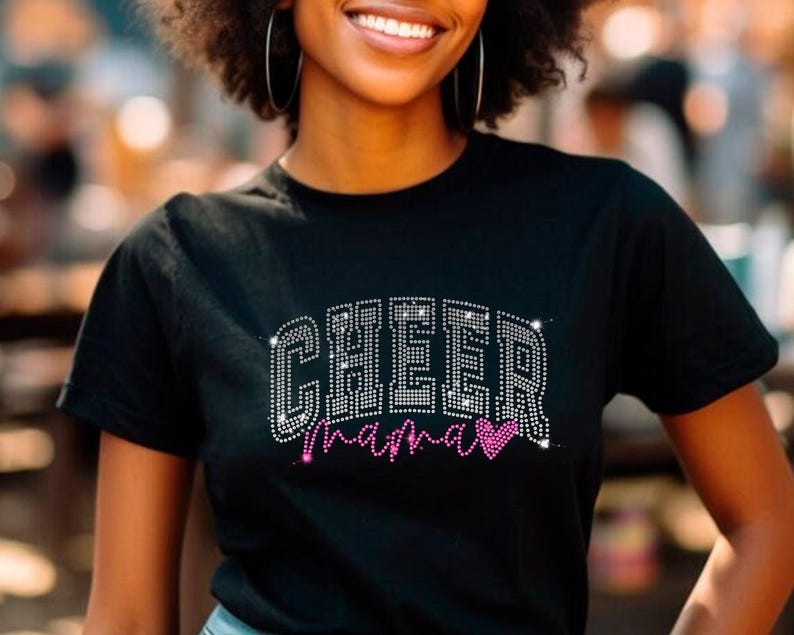 Op de afbeelding: Zwart T-shirt met een strass-ontwerp met de tekst "Cheer Mama" met een roze hart.