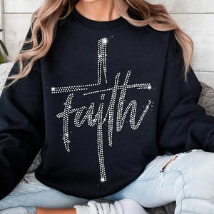 May include: Black sweatshirt with the word "faith" in a rhinestone design. The word "faith" is written in a cursive font and is overlaid with a rhinestone cross. The sweatshirt is a crew neck style.