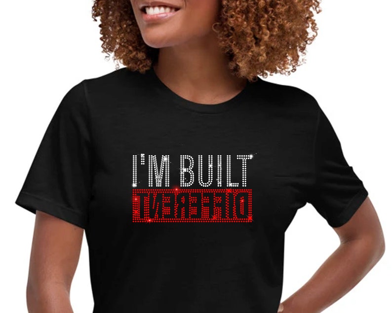 May include: Black t-shirt with the text "I'm Built Different" in white rhinestones. The word "Different" is in red rhinestones.