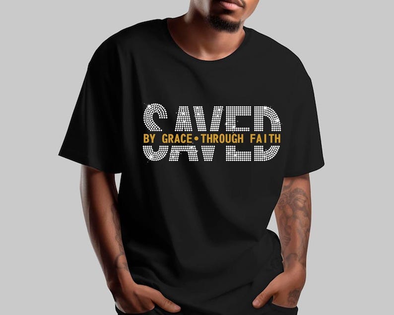 K&ouml;nnte beinhalten: Schwarzes T-Shirt mit dem Text "SAVED BY GRACE THROUGH FAITH" in Wei&szlig; und Gold. Der Text ist gestapelt, mit "SAVED" oben und unten. Das T-Shirt hat einen Rundhalsausschnitt.