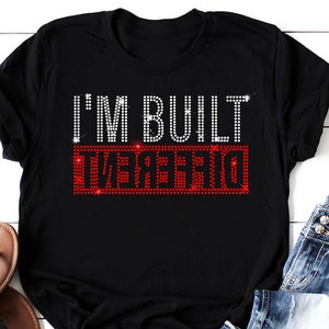 May include: Black t-shirt with the text "I'M BUILT DIFFERENT" in white and red rhinestones.