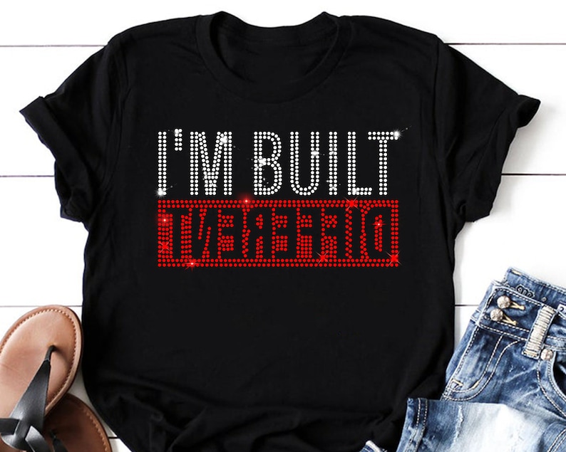 May include: Black t-shirt with the text "I'M BUILT DIFFERENT" in white and red rhinestones.