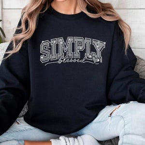 May include: Black sweatshirt with the words "SIMPLY blessed" in white rhinestones.