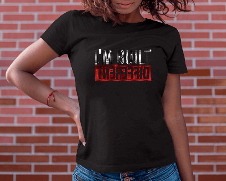 May include: Black t-shirt with the text "I'M BUILT DIFFERENT" in red rhinestones.