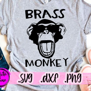 May include: A gray t-shirt with a black and white illustration of a monkey wearing sunglasses and the text "BRASS MONKEY" printed on it. The text "SVG .DXF .PNG" is printed on a pink banner below the image.