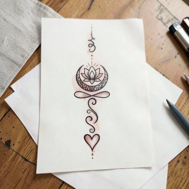 May include: A hand-drawn illustration on white paper featuring a lotus flower within a crescent moon, with a heart at the bottom. The design is in black ink with a hint of pink watercolor. The artwork is on a wooden surface.