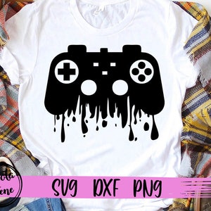 May include: A white t-shirt with a black graphic of a video game controller dripping with black paint. The text "SVG DXF PNG" is printed in pink at the bottom of the shirt.