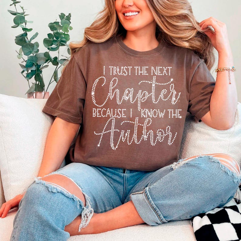 Puede incluir: Una camiseta marr&oacute;n con el texto "I trust the next chapter because I know the Author" en pedrer&iacute;a blanca.
