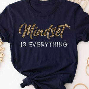 May include: A navy blue t-shirt with the text "Mindset is Everything" in gold glitter lettering.