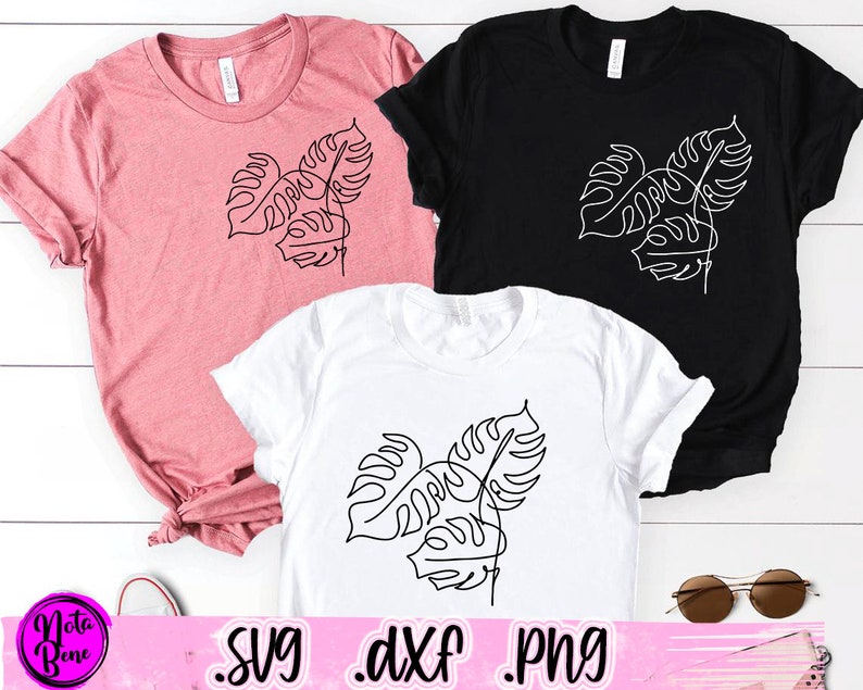 May include: Three different color t-shirts with a line drawing of a monstera leaf on each. The shirts are pink, black, and white.