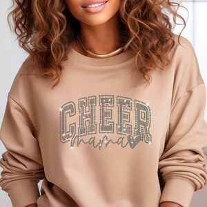 Op de afbeelding: Een beige sweatshirt met de woorden "CHEER mama" in zilveren strass.