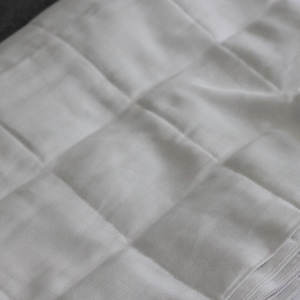 May include: A white quilted fabric with a smooth texture. The fabric is folded in a stack.