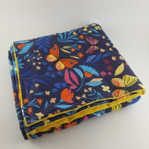 May include: A blue and yellow quilted blanket with a floral and butterfly pattern. The blanket is folded in half and has a yellow border.