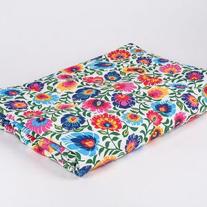 Könnte beinhalten: Weißer Stoff mit einem bunten Blumenmuster. Der Stoff zeigt ein sich wiederholendes Muster aus rosa, roten, gelben, blauen und grünen Blumen auf weißem Hintergrund.