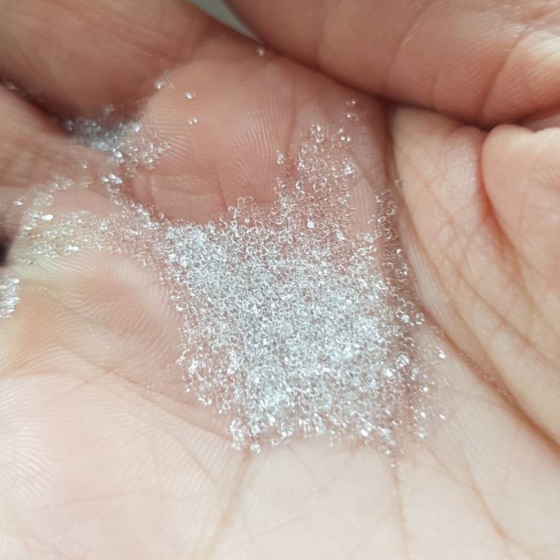 May include: A close-up of a hand holding a pile of small, clear, round beads.
