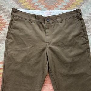 Pode incluir: Cal&ccedil;as de trabalho castanhas com fecho de bot&atilde;o e presilhas para cinto. As cal&ccedil;as t&ecirc;m bolsos frontais e um design de perna reta. O tecido parece ser um material dur&aacute;vel de cor s&oacute;lida.