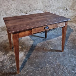 Könnte beinhalten: Ein rechteckiger Holztisch mit einer Schublade und vier sich verjüngenden Beinen. Der Tisch ist aus dunkelbraunem Holz gefertigt und hat einen Metallgriff. Der Tisch ist ca. 76 cm lang, 61 cm breit und 76 cm hoch.