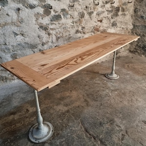Op de afbeelding: Een rechthoekige houten tafel met een lichtbruine afwerking. De tafel wordt ondersteund door vier metalen poten met een witte, verweerde afwerking. De tafel is ongeveer 183 cm lang en 91 cm breed, geschikt voor een eet- of werkruimte.