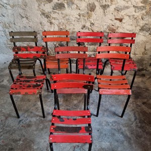 Könnte beinhalten: Eine Sammlung von Vintage-Metallstühlen mit roten und orangen Holzlatten. Die Stühle haben schwarze Metallrahmen und weisen Gebrauchsspuren auf, was ihren antiken Charme unterstreicht. Die Stühle sind in einer Gruppe angeordnet.