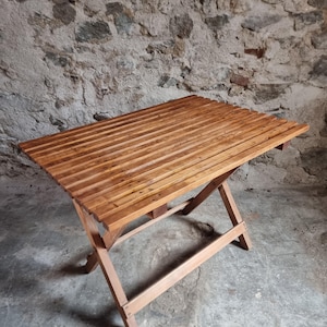 Op de afbeelding: Een opvouwbare houten tafel met een lattenblad. De tafel is gemaakt van lichtbruin hout en heeft een kruisvormig onderstel. De tafel is ongeveer 76 cm lang en 51 cm breed.