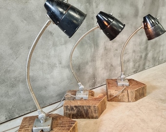 Peut inclure: Trois lampes de bureau industrielles vintage avec des abat-jours en métal noir et des bras réglables en argent. Chaque lampe est montée sur une base en bois épaisse.