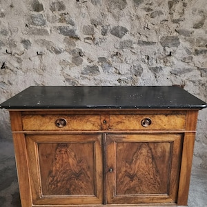 Könnte beinhalten: Ein hölzernes Sideboard mit einer dunklen, schwarzen rechteckigen Platte, zwei Schubladen mit runden Metallgriffen und zwei unteren Schranktüren mit sichtbarer Holzmaserung. Der Schrank ist aus hellbraunem Holz mit natürlichem Finish gefertigt.