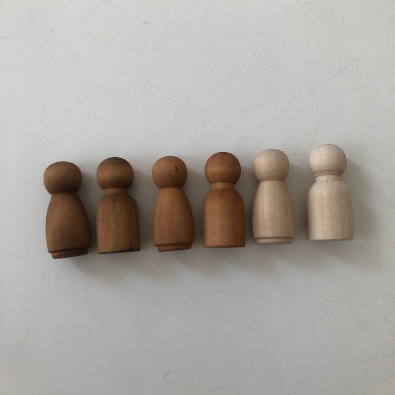 May include: Seven wooden peg dolls in a row, painted in various shades of brown and white. The dolls are all the same size and shape, with a round head and a simple body.
