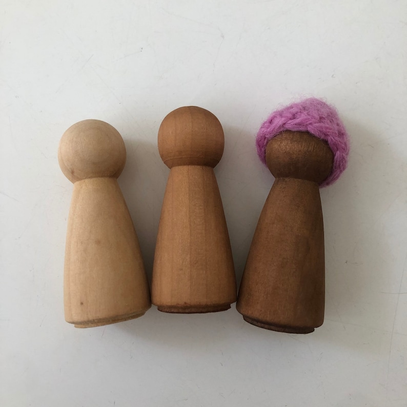 May include: Three wooden peg dolls, one with a pink knitted hat. The dolls are all different shades of brown.